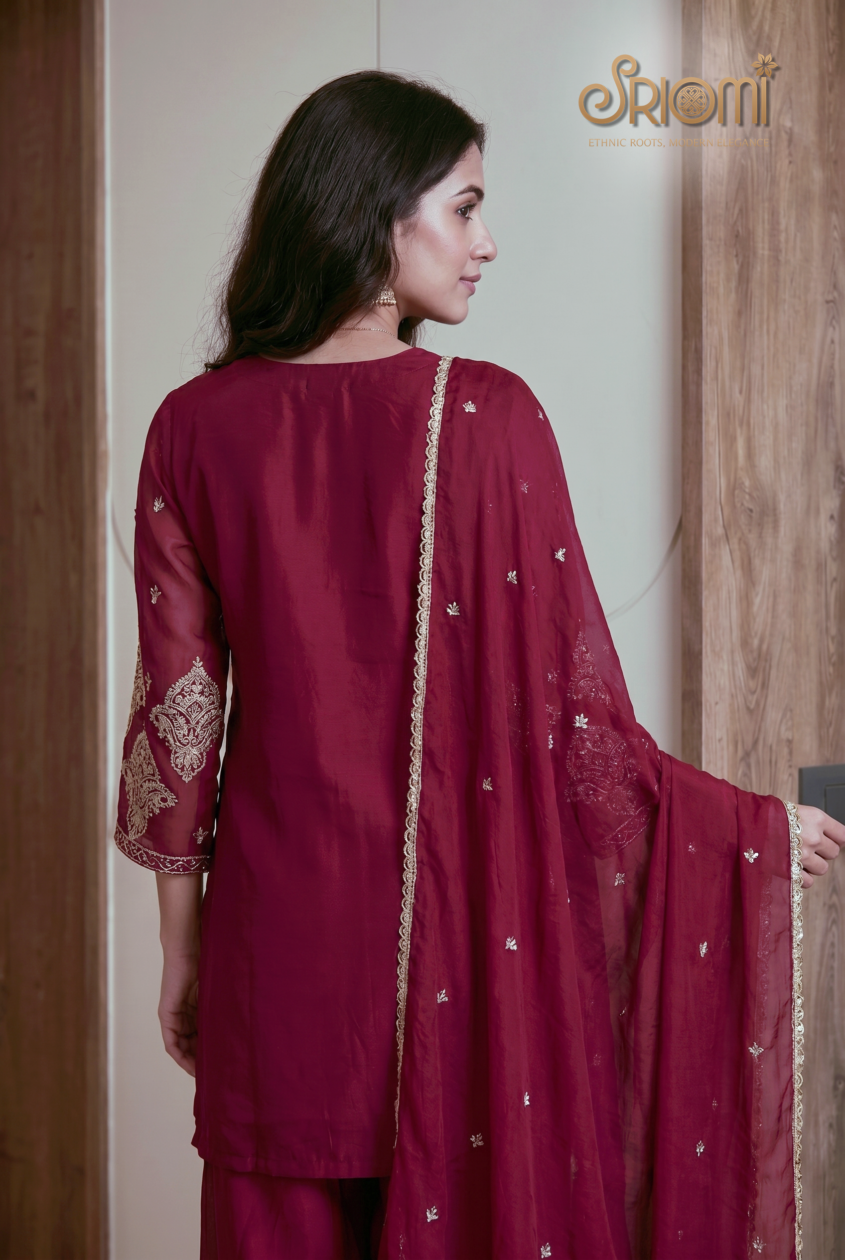 Woman wearing a maroon traditional outfit with white embroidery, holding a matching dupatta.