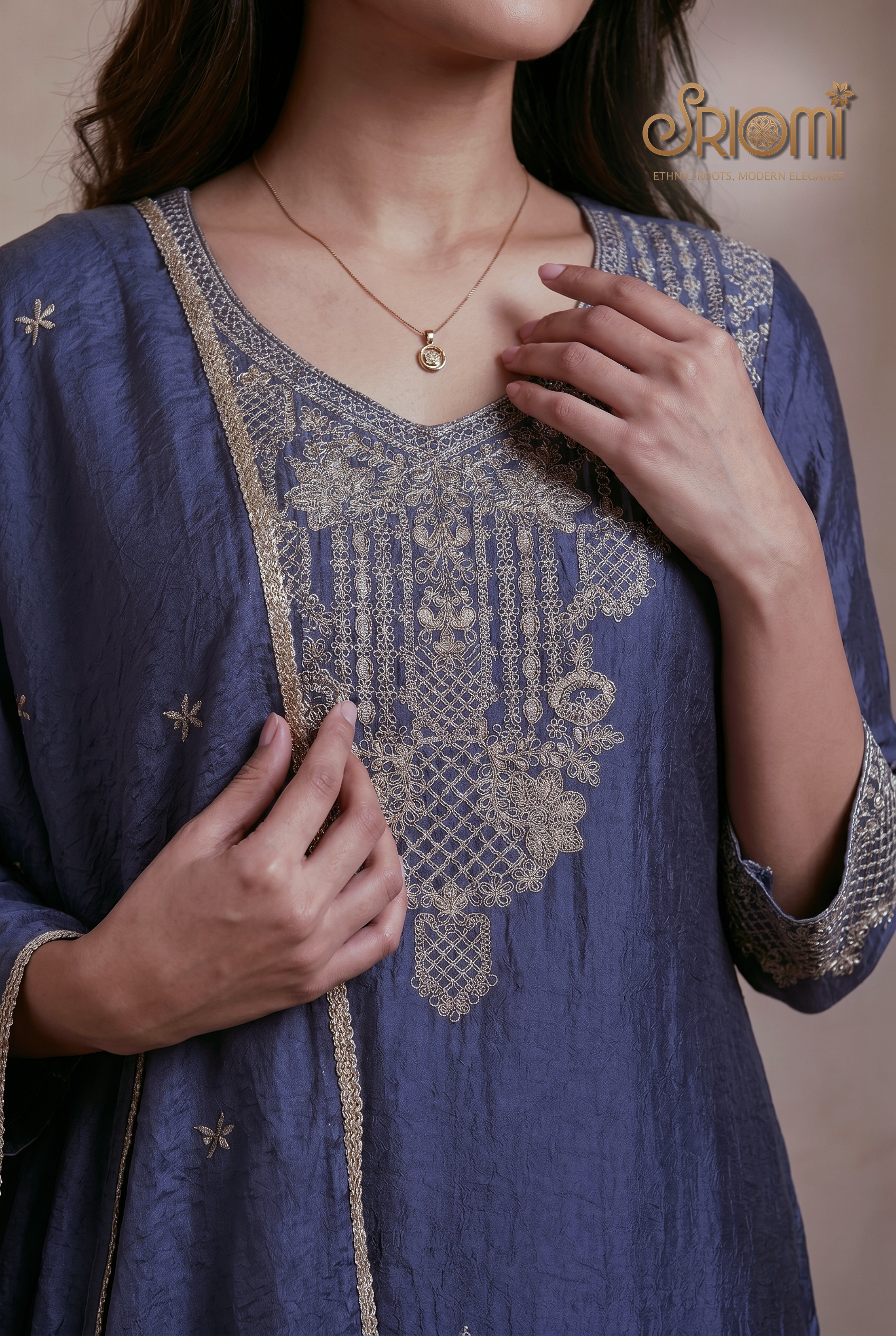 Blue embroidered garment with gold detailing, worn by a person, on a neutral background.